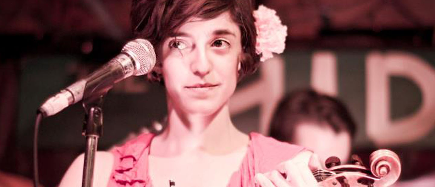 woman with flower in her hair holding a violin about to sing into a microphone at the Hideout
