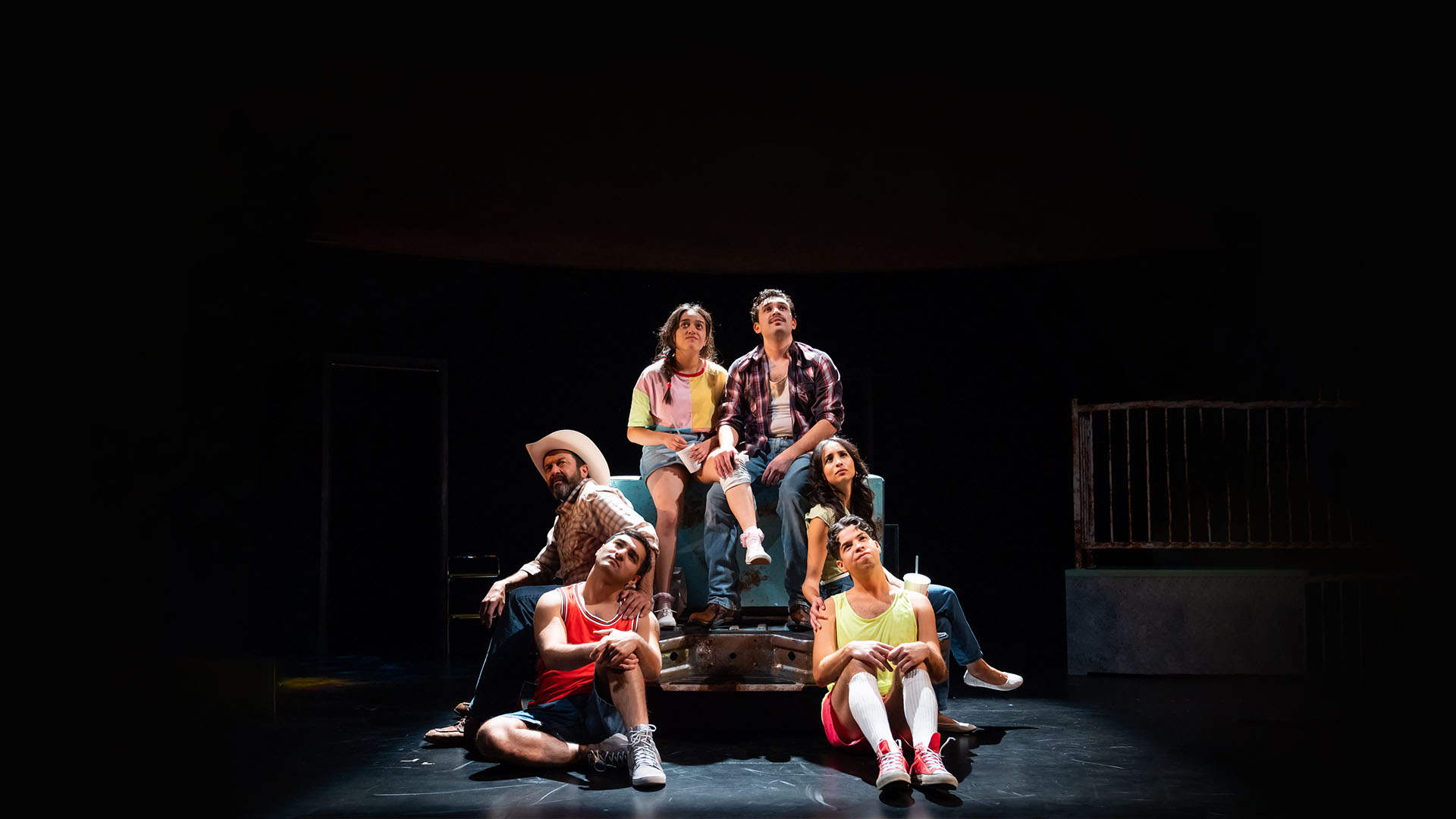 Six people sitting on a multi-level platform under a spotlight in stage.