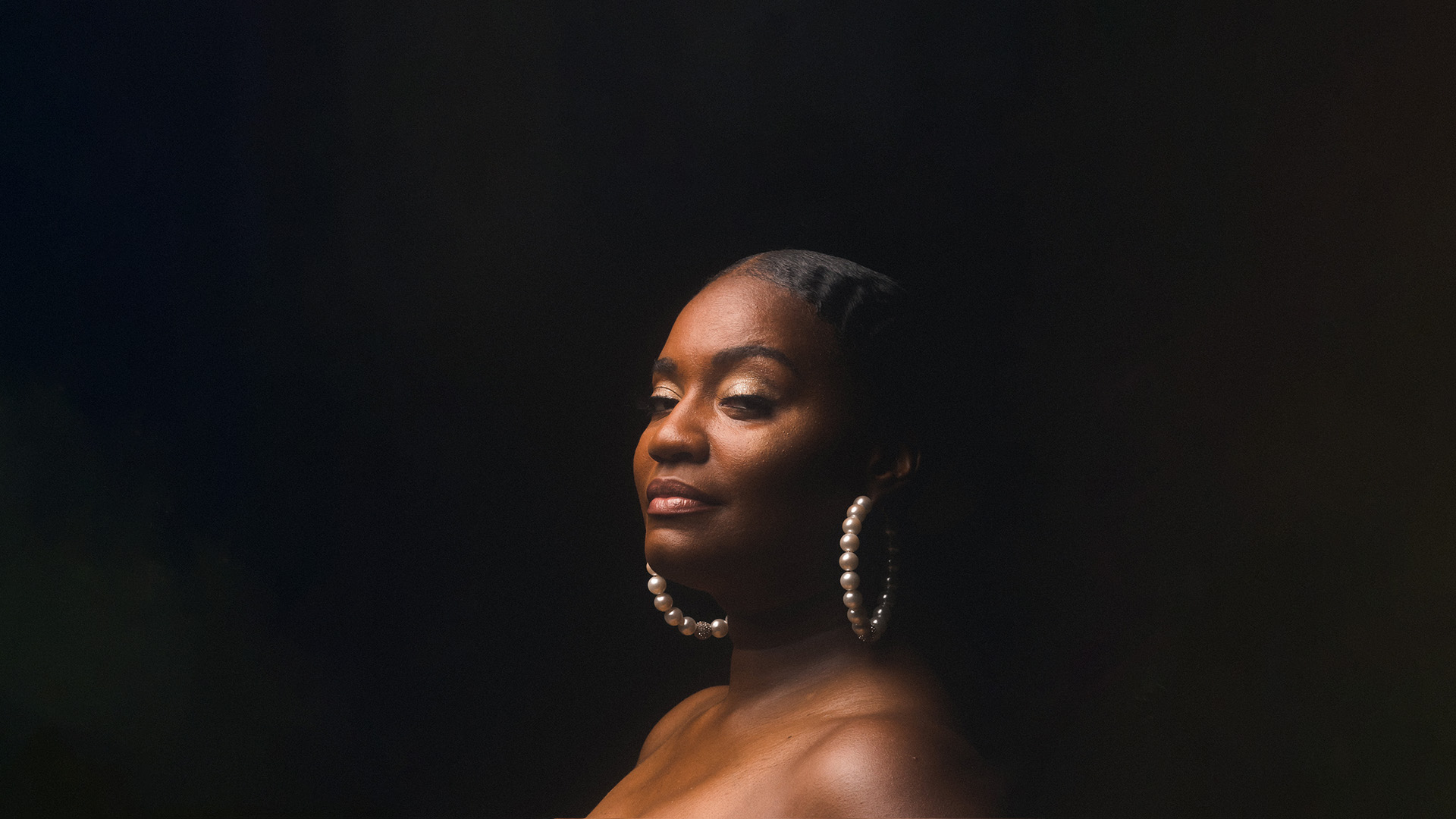 Beautiful, brown skinned, voluptuous woman with natural hair in a gold crown and against a black background.