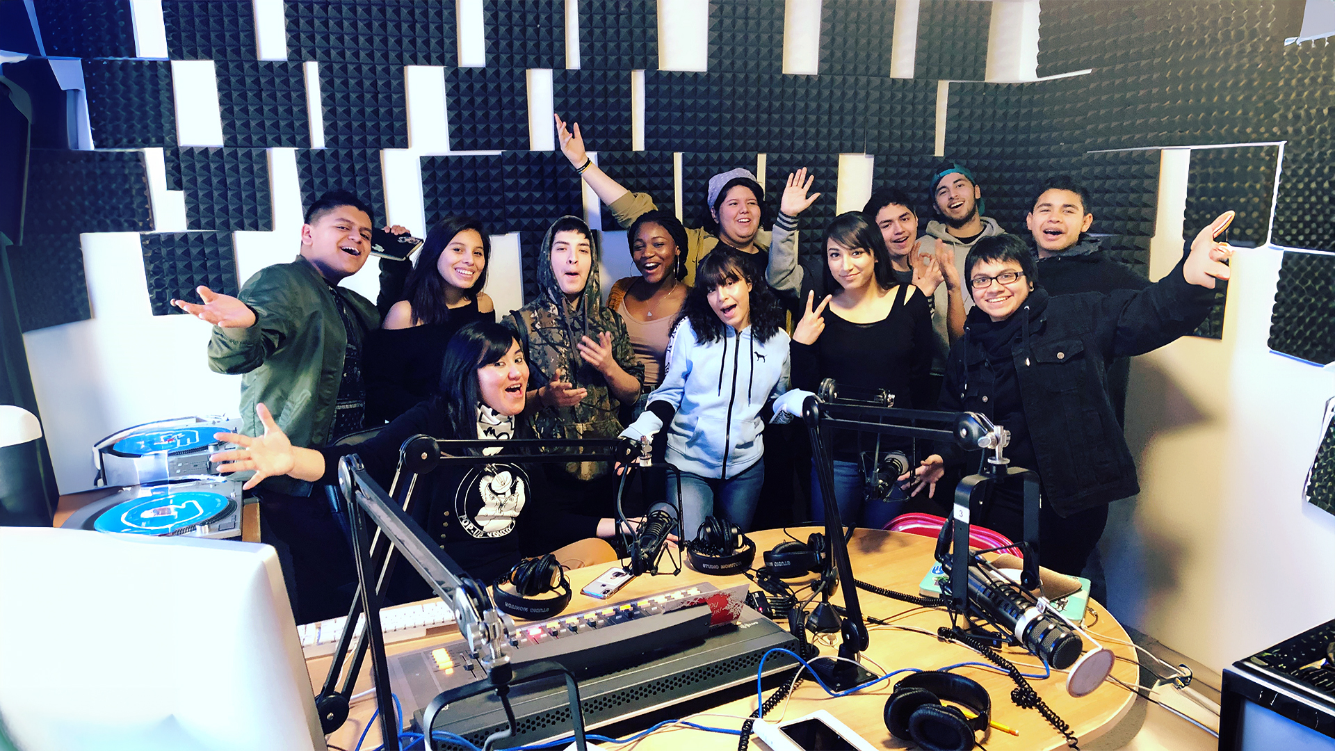 group of students and teacher pose in radio booth