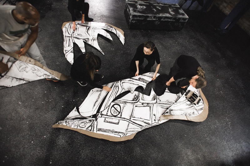  Five people putting a large scale drawing together on the ground. 