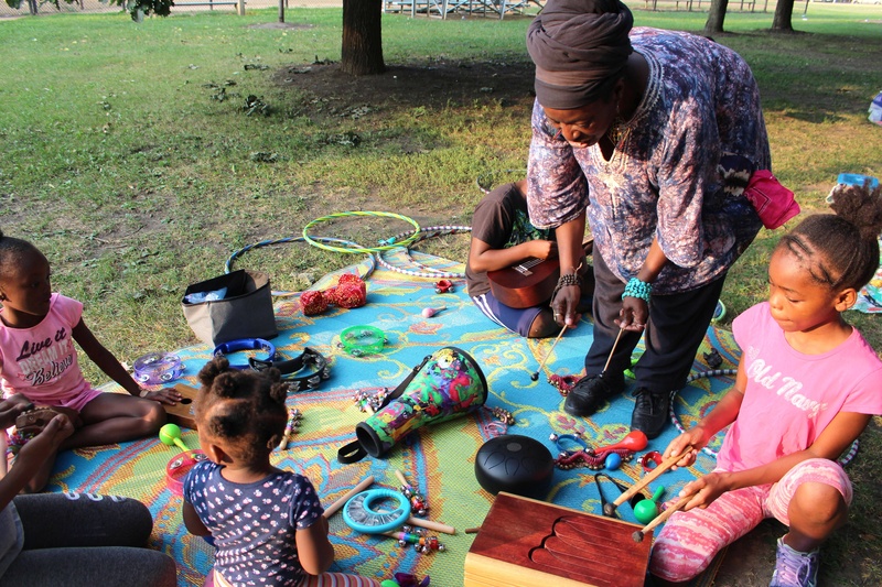  Teacher stands in the middle of five children and instructs them on how to play percussion instruments. 