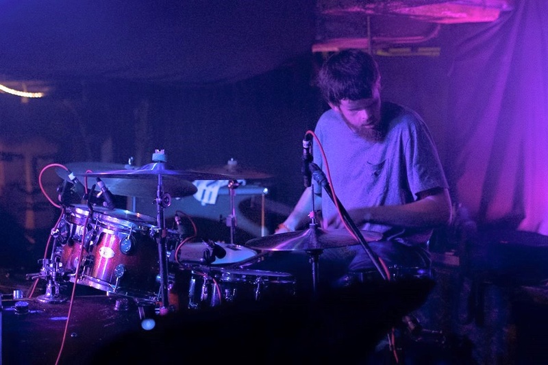  Tommy playing drums on a low lit performance stage 