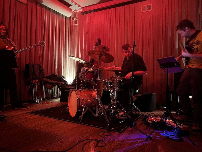 A White man with a beard plays the drums in a red lit restaurant