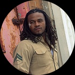 Black man with locs and white face paint looks left