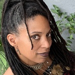 Person with long dark brown locs with salt and pepper gray on the sides and brown eyes