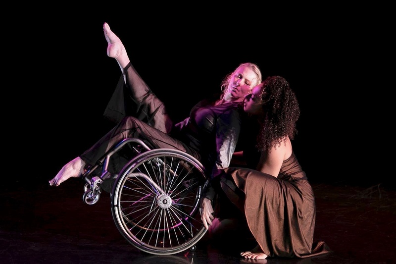  Ladonna in wheelchair with one leg lifted, tilting back and supported by another dancer 