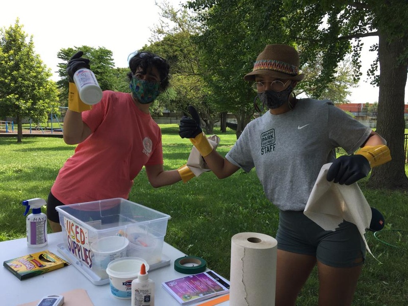  Two figures wearing face masks and gloves, seen sanitizing tools for a post-lesson clean up 