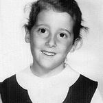 A young white second-grader with an open smile, wispy hair, and a peter pan collar (catholic school uniform)