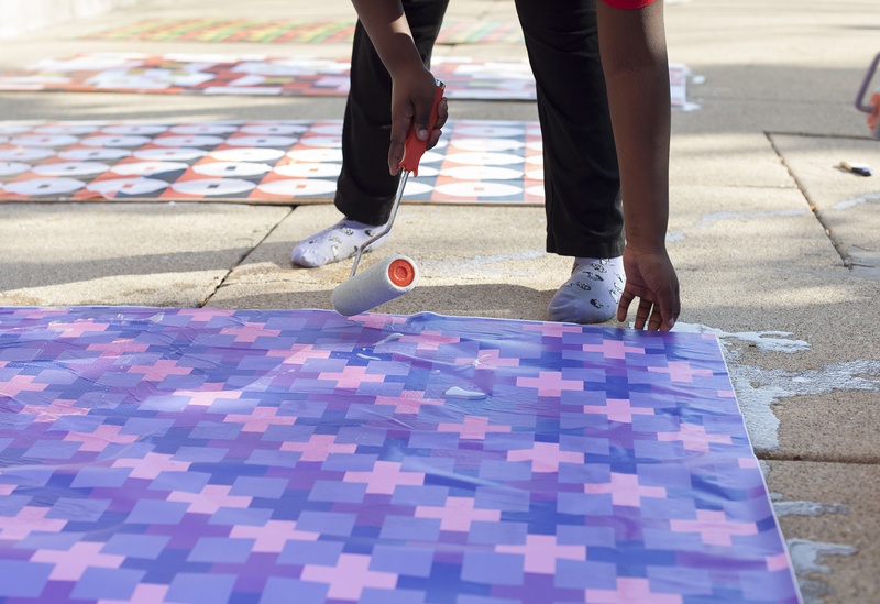  Person paints paper on the sidewalk with a roller brush 