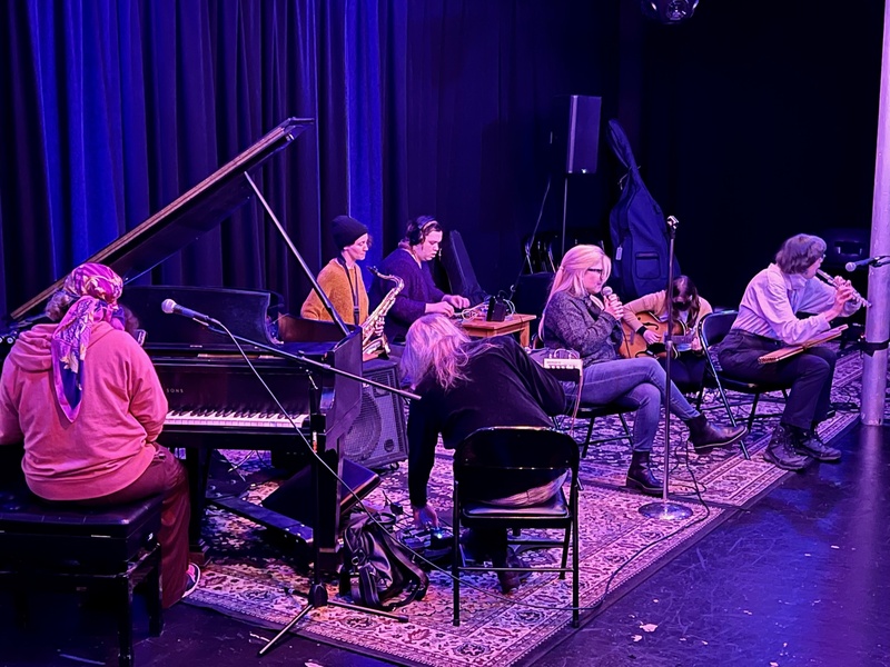  Image of five musicians on small stage play improvised jam session. 