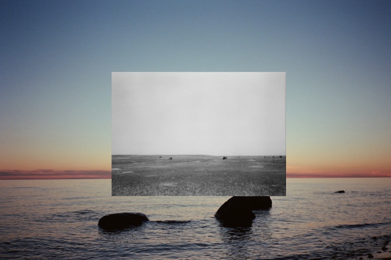  Composite image with an archival grayscale image of a barren landscape, super imposed on another image of a soft sunset horizon on a calm body of water 