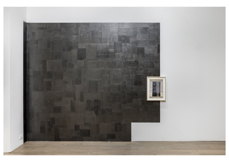  Partial view of a series of walls that have been reconfigured visually by a membrane made of thin shimmery graphite film. This wall is a host to a smaller fabric collage of a picture of cloth’s selvedge with embroidery on top. 