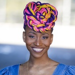 Black woman with multicolored braids adorning the top of her head, smiling at the camera