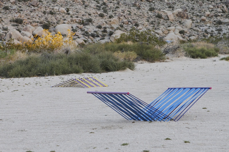  Two geometric sculptures peak out of sand and mimic beach chairs without legs 