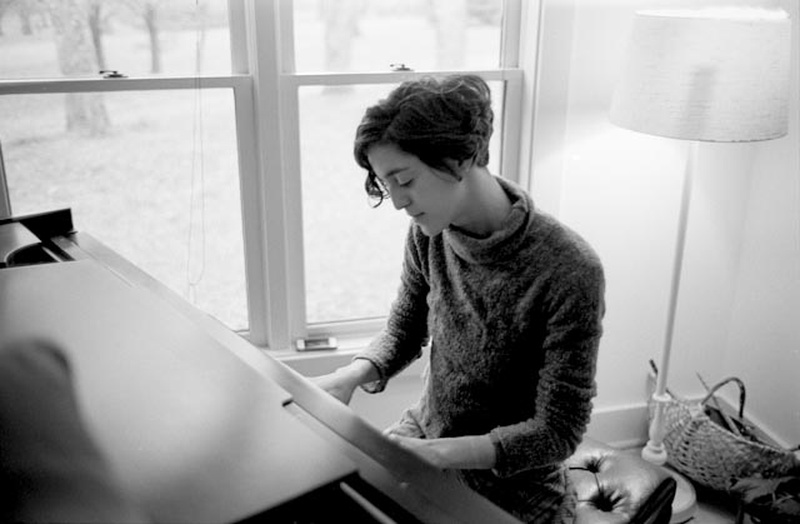  black and white image of a woman in a fuzzy sweater playing a grand piano 