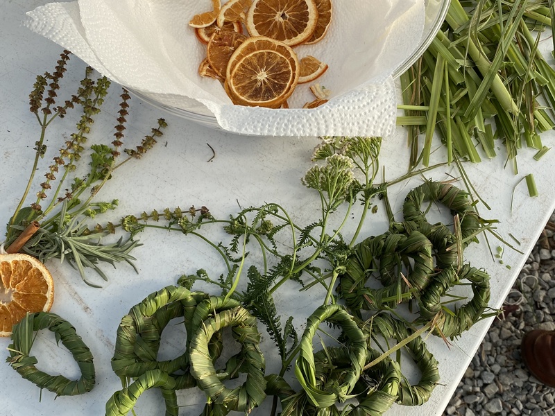  Image of woven strands of lemongrass and dried orange slices set upon a white table 