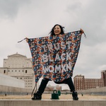 Aram, a Korean American womxn, is holding a protest banner that says TRUST BLACK WOMXN and is standing on top of a building