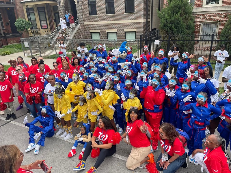  large group of black children in yellow, blue, and red outfits look at the camera while holding up peace signs 