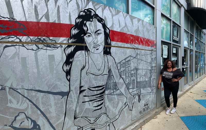  Graffiti drawing of a female figure on a wall with a Black Mexican woman in the background leaning against the wall 