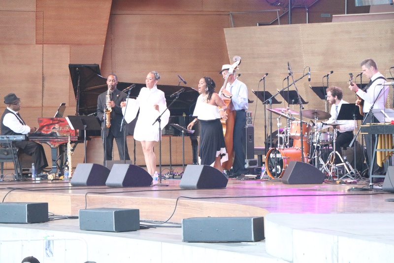  Group of musicians playing instruments or singing into microphones on an outdoor stage 