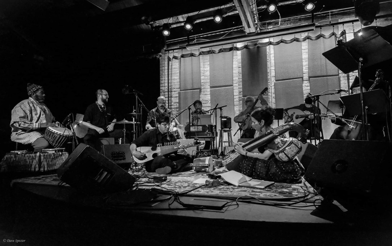  black adn white photo of musicians sitting on stage playing sitar and drums. 