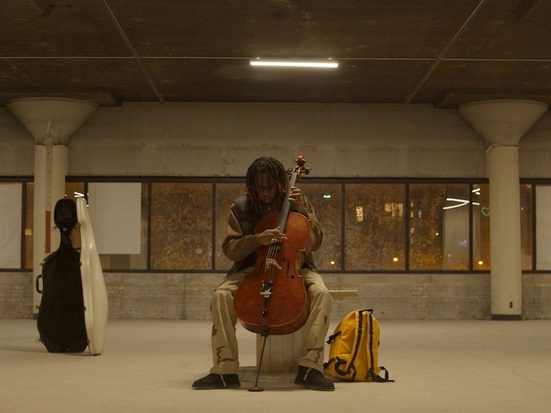  Person with cello sits in the middle of gallery space and plays 