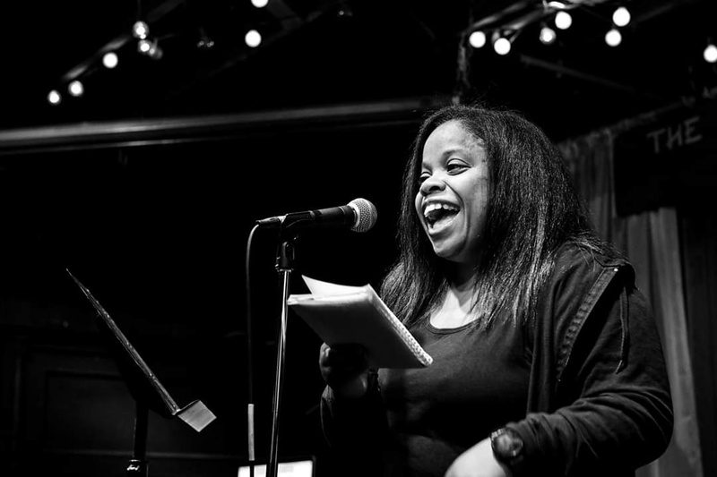  A Black and white photograph of a black woman smiling and speaking into a microphone. 