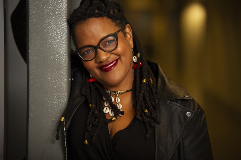  black woman wearing long locs, cowrie shell necklace and black leather jacket 