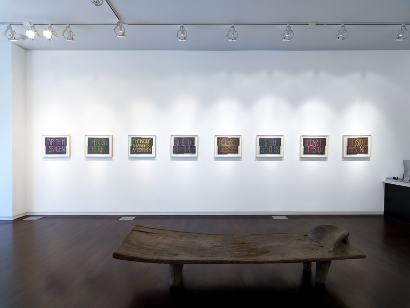 An image of a gallery wall with rectangular works consisting of embroidered text in different colors. The embroidered letters are sewn on a graphite background. The works are all the same size. 
