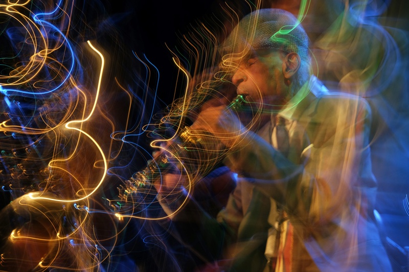  A saxophone player with a jaunty hat erupts in green and blue sound light patterns 