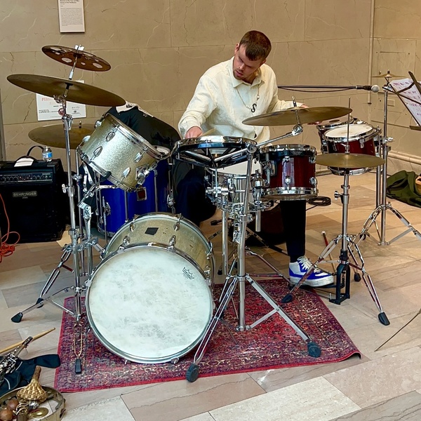 A White man with a beard plays the drums