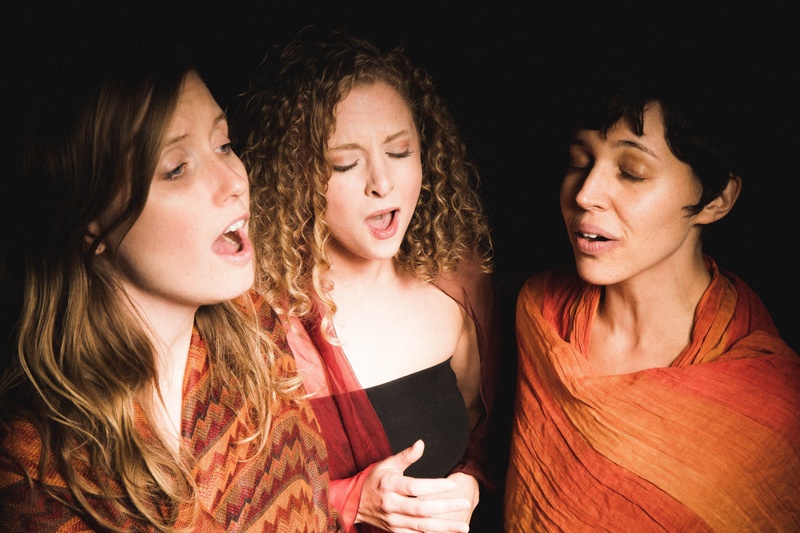 Three women appear mid song. Their mouths are wide and they appear pensive and focused. 