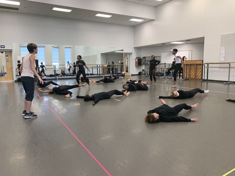  Dancers dressed in black leotards and tights flailing about on the floor in a studio with mirrors 