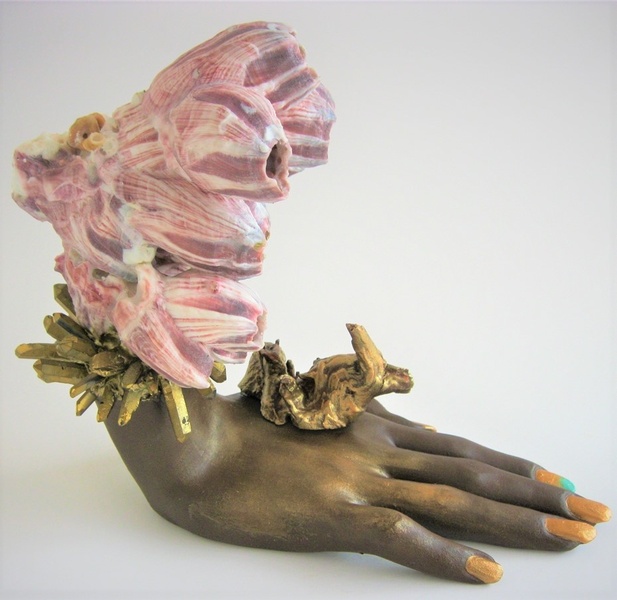  dark brown painted vintage mannequin hand laid flat, wrist upright with a pink and purple barnacle cluster extending upward from top of wrist; gold-painted twisted piece of cactus wood extending from top of hand and quartz points extending out from wrist 