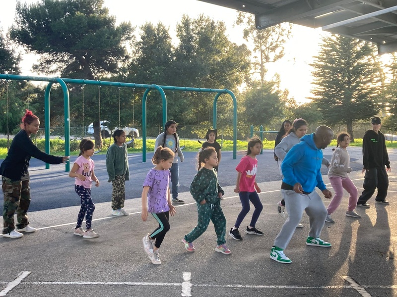  grou pof children stand on playground and learn dance 