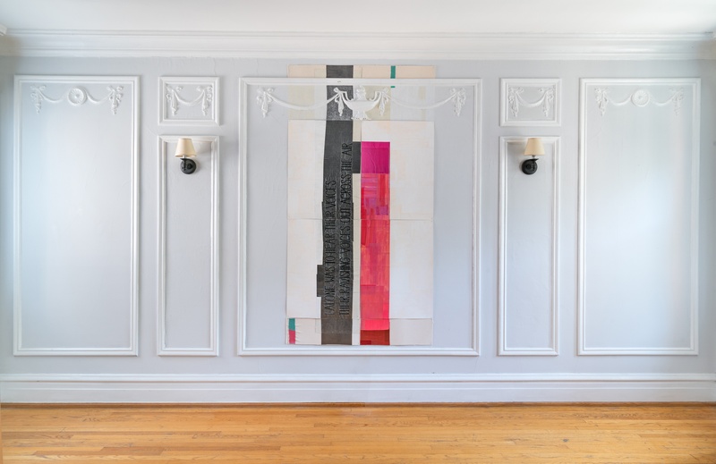  View of a room with a site-specific work on paper, architecturally framed by pre-existing plaster molding.  The work has pink, white and graphite hues. Black letters have been embroidered on the graphite section. 