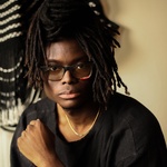 Black man with long dread locs, brown eyes, and glasses