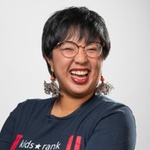 Asian American person with black hair, glasses, and a big smile
