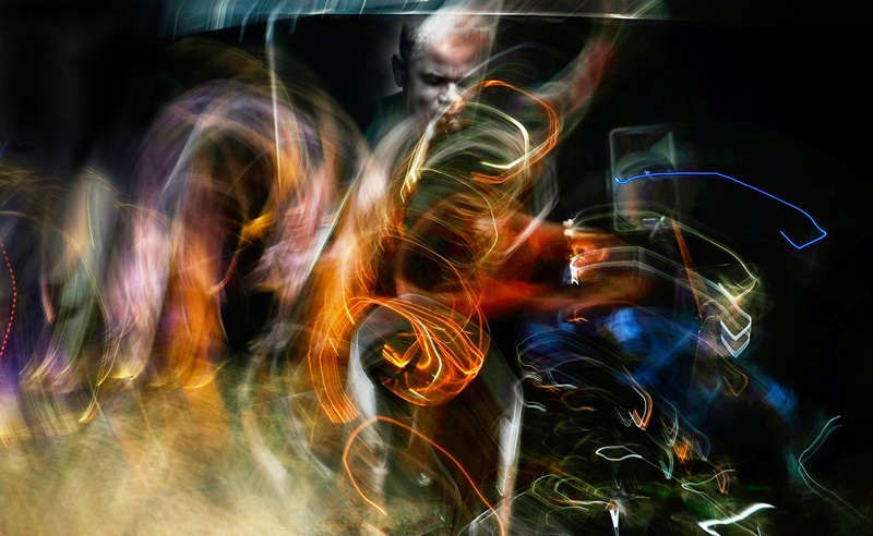  A saxophone player is in the center of  gold and orange and green swirls of energy emanating from his horn 