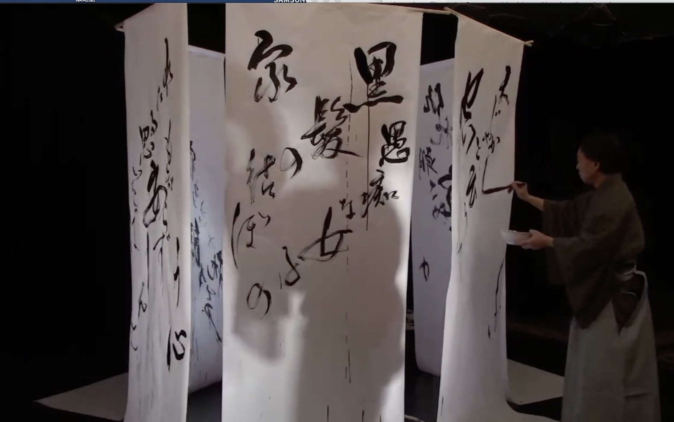 Calligrapher writes on a hexagonal paper cage as a shadow  of a dancer is within. 