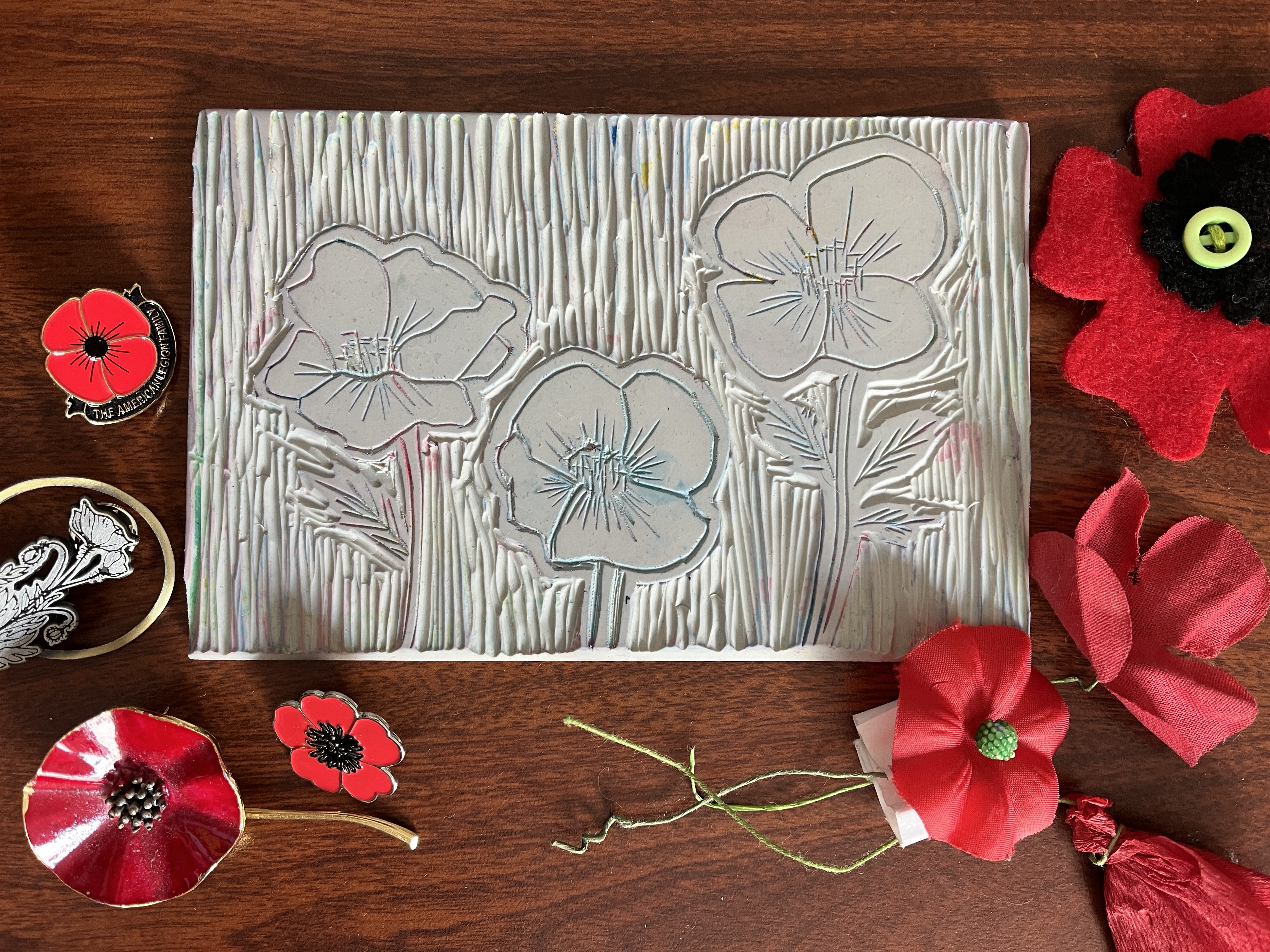  linoleum block with three poppies surrounded by variety of poppy pins 
