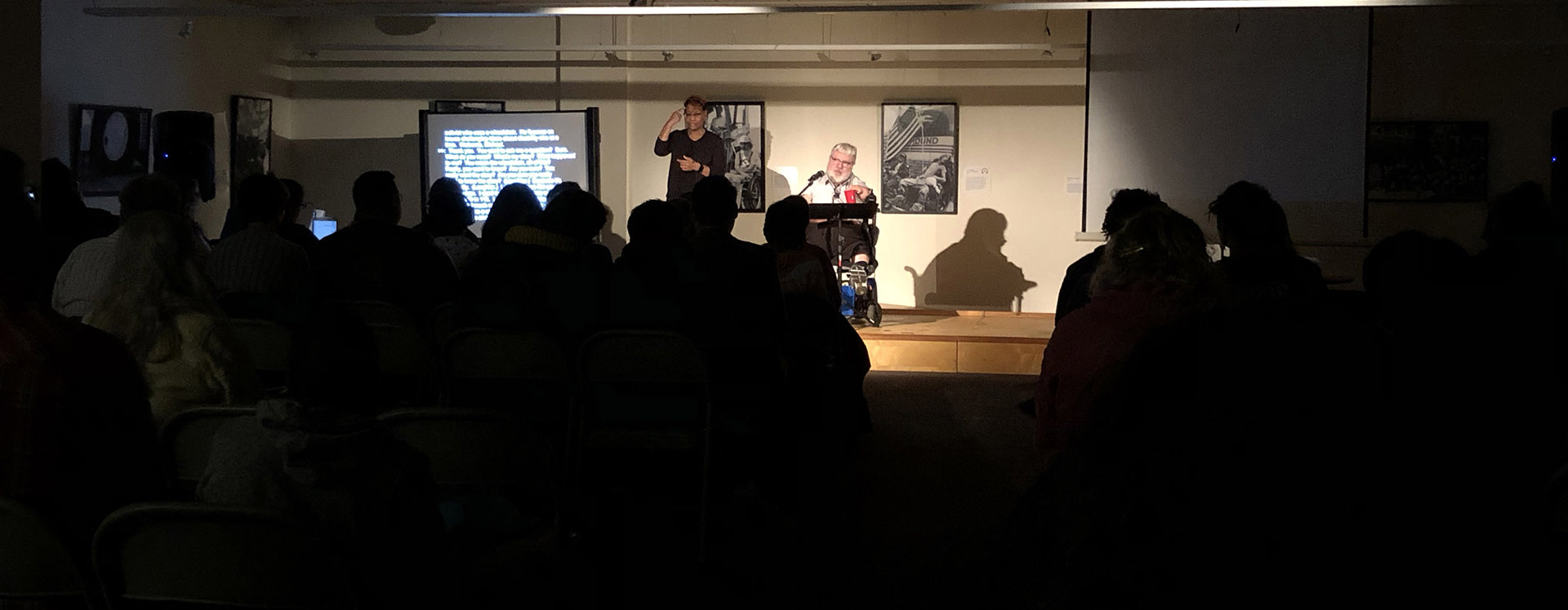 Robert on stage with an ASL interpreter in front of a dark crowd