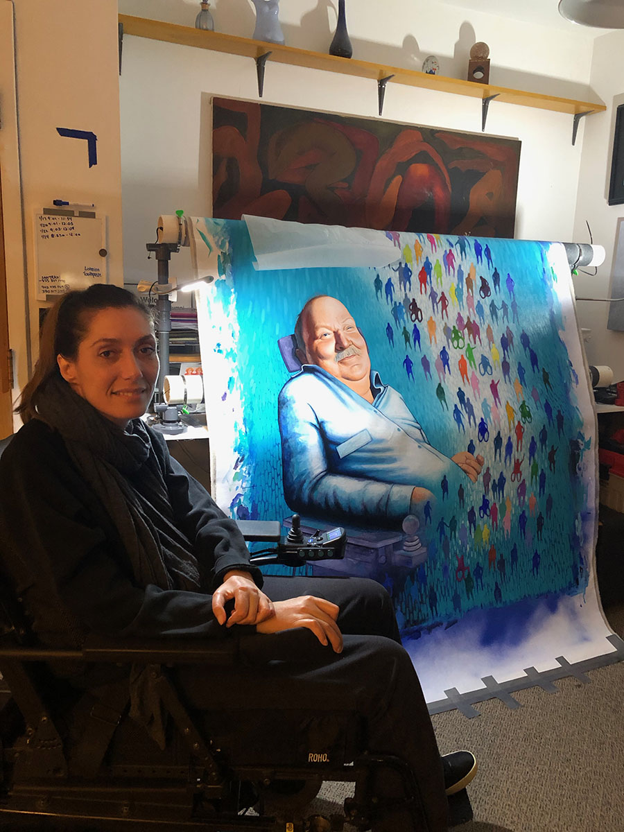 Mariam posing in front of a painting of a man in a wheelchair surrounded by many figures.