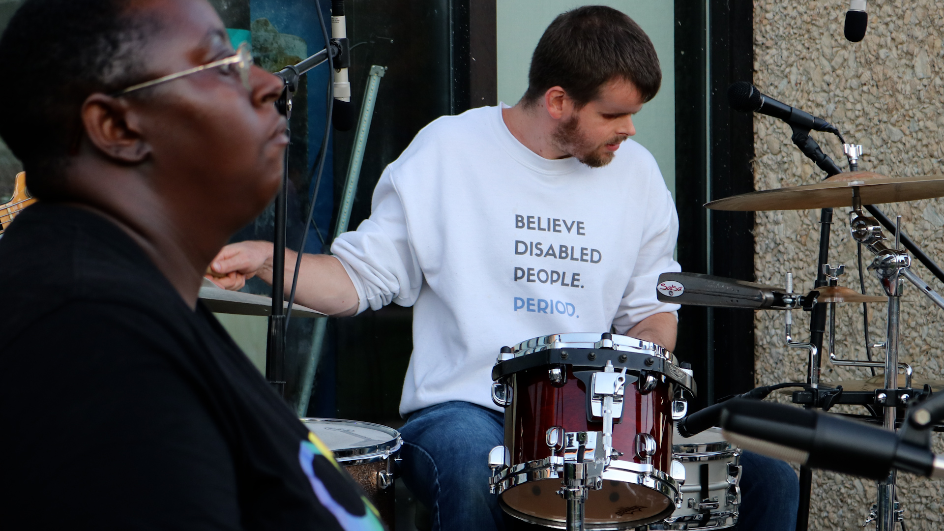 Tommy Carroll drumming outside with a shirt that says Believe Disabled People Period