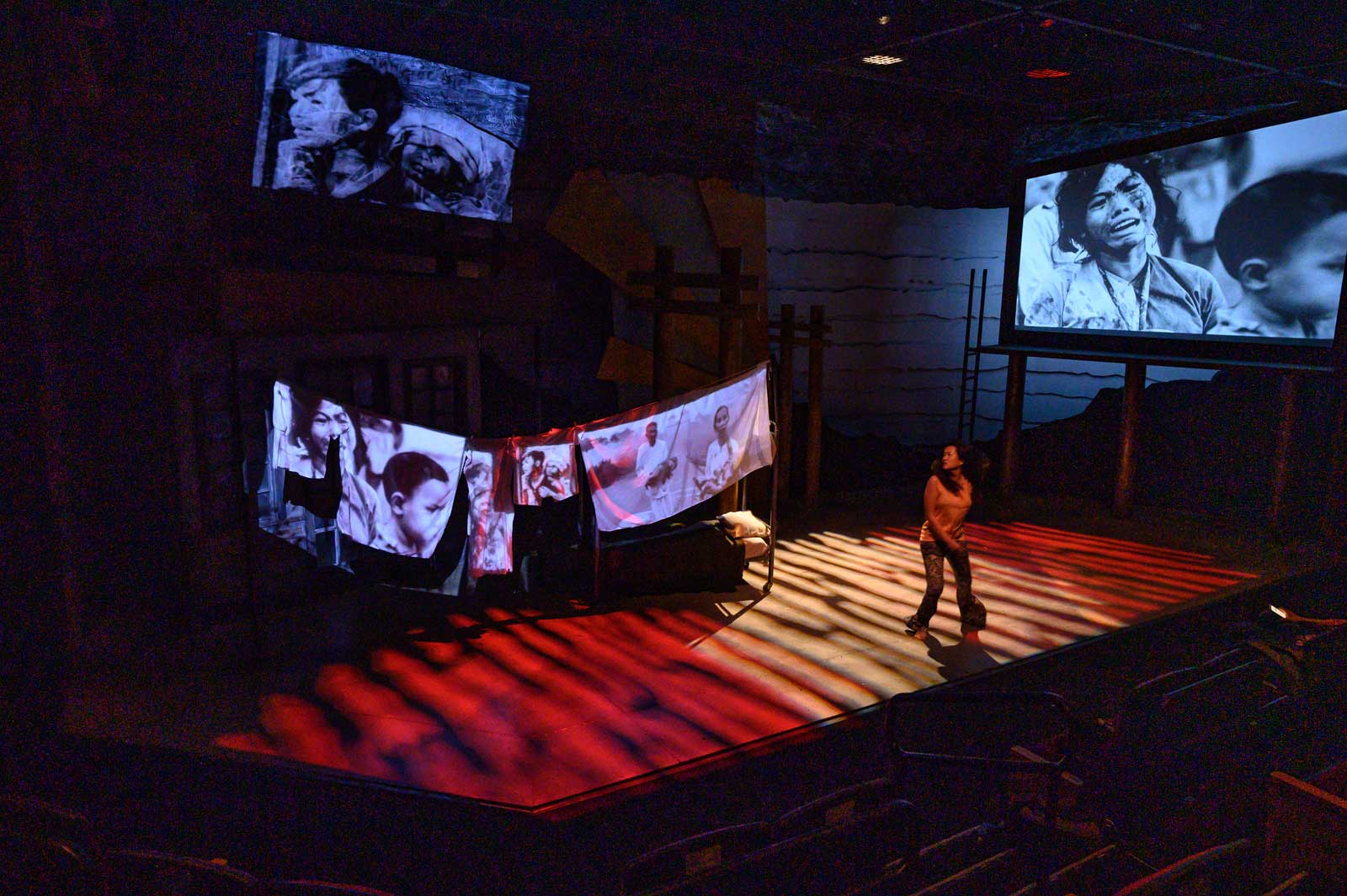 A person on stage looking at large projections of war.