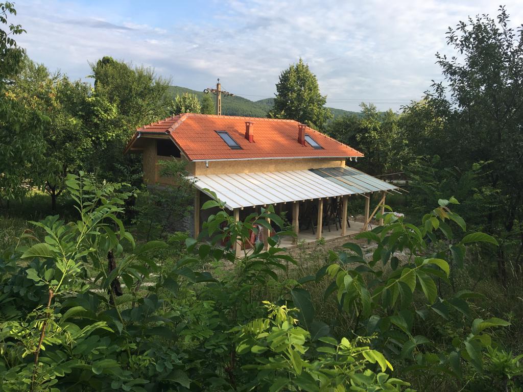 Small house with orange new roof set within a forested hillside